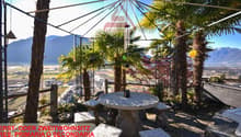 Outdoor terrace with seating area, table, pergola, palm trees, mountainous background, scenic landscape