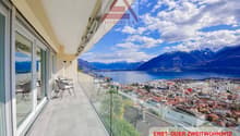 Balcony with glass railing, table and chairs, glass doors, scenic mountain and lake view