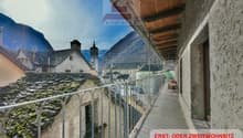 Balcony with stone walls, metal railing, roof with moss, street, view of a mountain and buildings.
