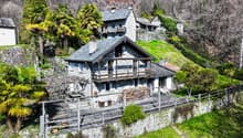 Stone house, multiple levels, wooden balcony, surrounded by trees, mountain view