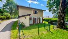 Detached house, beige exterior, green fence, driveway, garden, trees, bushes, clear sky