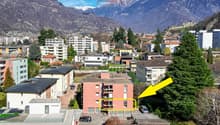 Aerial view of a residential area with a highlighted apartment building, surrounded by other buildings, trees, and mountains in the background.