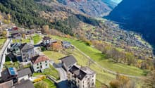 Mountain village with several houses, green fields, and a valley in the background