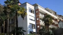 Multi-story apartment building with balconies, surrounded by palm trees and greenery