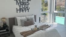 large bed with white duvet, grey and white pillows, black nightstand with books, lamp, round white lampshade, large windows overlooking pool