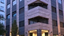 Modern apartment building, multiple floors, glass windows, entrance with lights, shrubs and trees in front