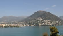 Scenic view of a mountainous town situated on the shores of a large lake, with blue waters and a clear sky in the background.