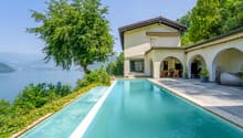 Two-story villa with a swimming pool, surrounded by lush greenery and overlooking a lake. The villa has a terrace and large windows, providing a scenic view of the natural landscape.