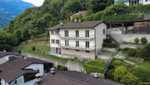 Detached house, multiple floors, tiled roof, exterior balconies, walled terrace, neighboring houses visible, situated on a slope with retaining walls