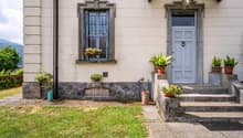 Traditional house, cream painted exterior, stone wall base, front door with window, step, several plants and flowers in front