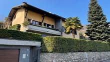 Detached house, beige painted exterior, small balcony, large garage, landscaped hedges, mature trees