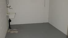 Empty basement, white walls, gray floor, white sink, small sink drain, plumbing pipes