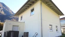 Single-family home, 2 stories, white exterior, small garden with grass, mountain backdrop