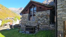 Old house made of stone, with a solar panel on the roof, wooden door, two windows, surrounded by lush green grass