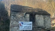 Old stone house, located on a hillside, with a slate roof, surrounded by trees, with a sign indicating it is for sale