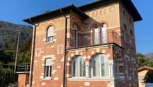 Villa with brick walls, wooden entrance, large arched windows, balcony, lush green surroundings