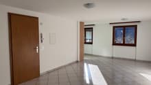 Empty room, white walls, tiled floor, two windows, wooden door, two switches, and telephone mounted on the wall.