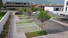 paved parking area with grass, concrete flowerbed, and two parked cars, building at a distance with mountain