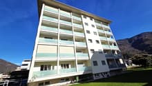 Apartment building, 6 floors, balconies on each floor, garden in front, mountains in the background