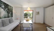 modern living room with white couch, dining table, white chairs, white walls, wooden floor, balcony, white curtains, white lamp, picture on wall