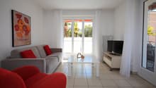 modern living room, gray sofa, red armchair, white coffee table, TV, white curtains, balcony, view of trees