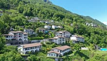 Hillside residential area with multi-story buildings, balconies, and parking spaces surrounded by lush green vegetation and mountains