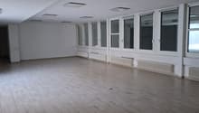 large room with white walls, wooden floors, windows, heating radiators, ceiling lights