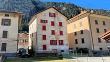4 story house, red shutters, beige and stone wall, small garden, surrounded by green mountains