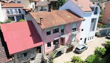 pink house with multiple balconies and red roof, two chimneys visible, large garden in front, street