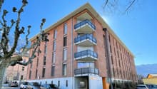 modern apartment building, brick exterior, balconies, street-level garage, several cars parked in front