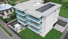3-story apartment building, solar panels on roof, blue balconies, surrounding greenery, parking area