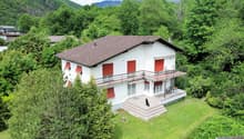 2 story house, white exterior, brown roof, balcony, large front yard, surrounded by trees, grassy area