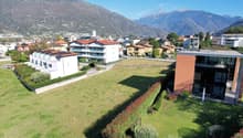 Aerial view of a residential area with several buildings, mountains in the background, and a large open field.