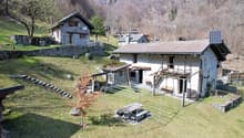 Stone house with solar panels, wooden benches, stone steps, and a metal structure with a table and benches