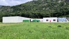 white building, green containers, red doors, large grassy field, mountain in the background
