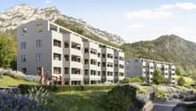 modern multistory building, surrounded by mountains, greenery, car access road, parking spaces