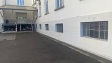 Empty parking lot beside a building, several windows, a garage door, several air conditioning units attached to the wall