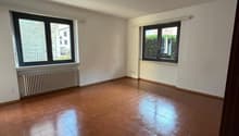 Empty room with tile flooring, white walls, two large windows with black frames, white radiators, and an electrical outlet.