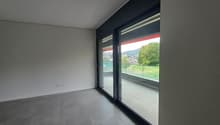 Spacious room with large windows offering a scenic view, grey tiled flooring, and dark-colored walls.