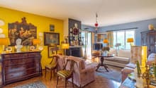 Living room with fireplace, yellow and blue walls, a TV, multiple paintings and frames, a carpet, a desk, a couch, and chairs