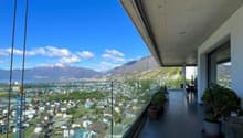 Terrace with glass railings, view of city and mountains, table, chairs, plants, and trees