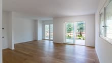 Spacious living room with large windows, hardwood flooring, and access to a balcony or terrace overlooking the surrounding neighborhood