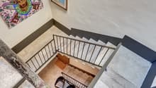 Two-story house, marble floors, staircase, black modern chairs, framed painting on the wall.