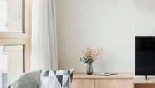 light-filled room, wooden chair, TV, wooden side table with flowers, light curtains, light wooden floor