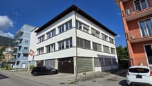 Three-story building, white exterior, garage, red Swiss flag on the wall