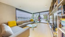 modern living room with large windows, gray sofa, glass coffee table, wooden floor, TV, bookshelf