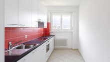 Modern kitchen with white cabinets, red tile backsplash, stainless steel sink, and dishwasher. The kitchen has a window and tiled flooring.