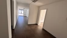 Empty hallway with brown tiled flooring, white walls, windows, and ceiling lighting
