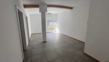 Empty room with white walls, gray tiled floor, wooden beam on ceiling, window with blinds, and an air conditioning unit.