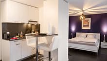 The image shows a studio apartment with an open-concept layout. The kitchen area features white cabinets, a black countertop, and a dishwasher. The living and sleeping areas are separated by a partial wall, with a bed visible in the bedroom section. The r